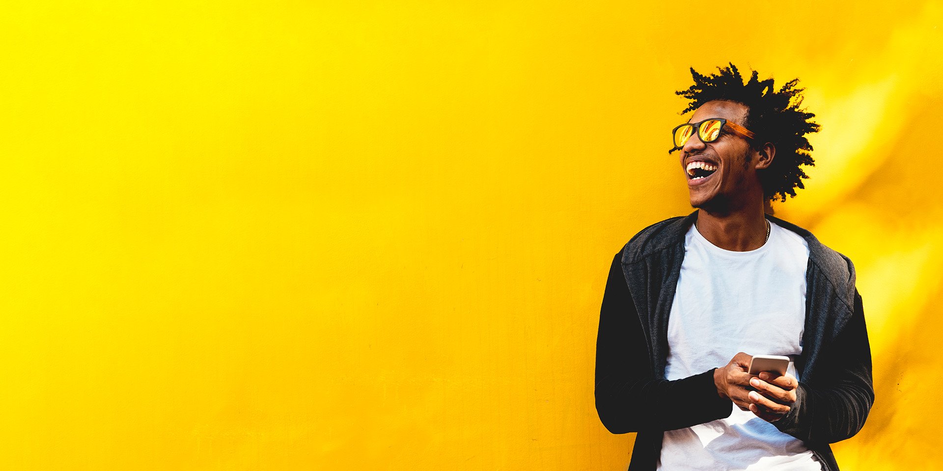 A happy man using his Desert Financial mobile banking app on his smartphone in front of a yellow background.