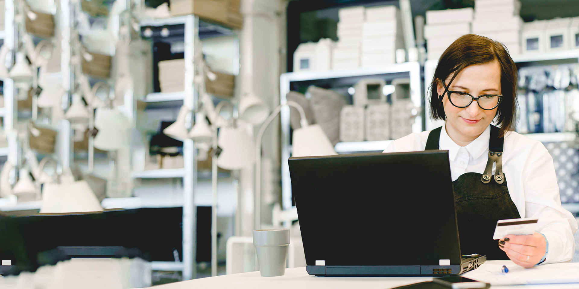 A store owner in an apron securely enters her business' Desert Financial credit card information into a laptop behind the counter.