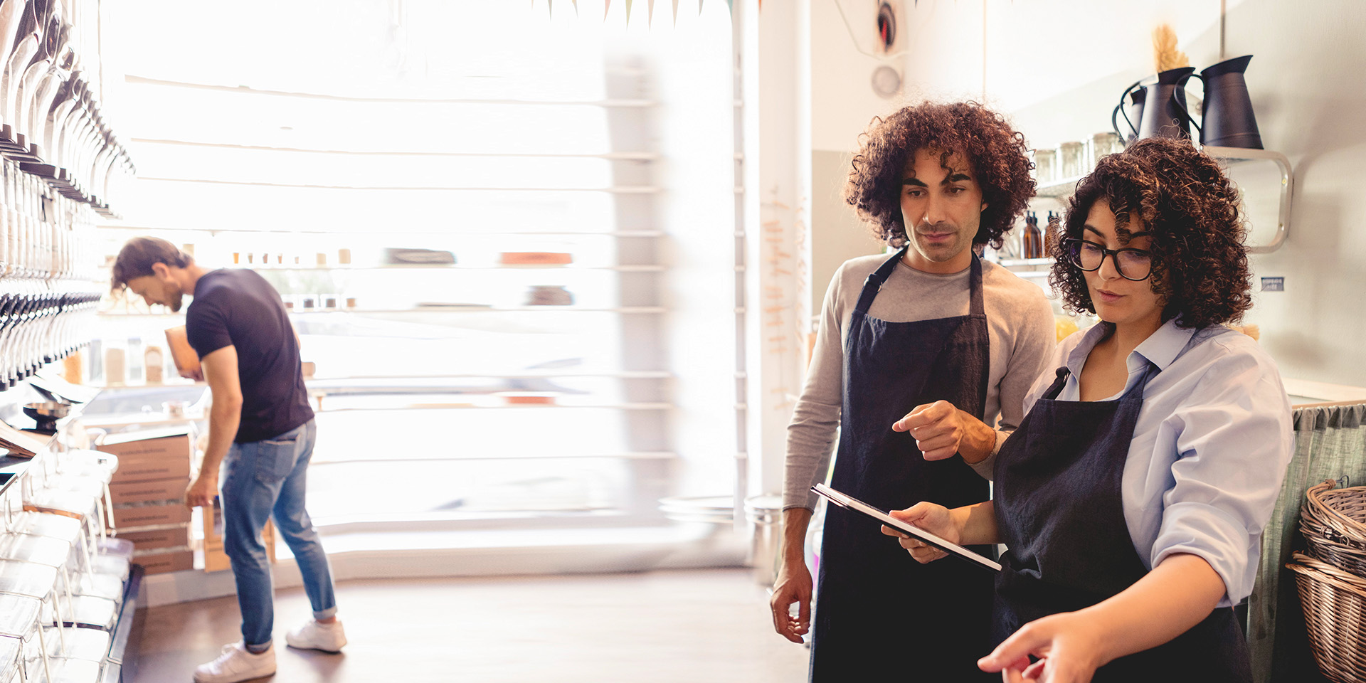 Two workers, in aprons, using a tablet to efficiently organize the shelves in the store.