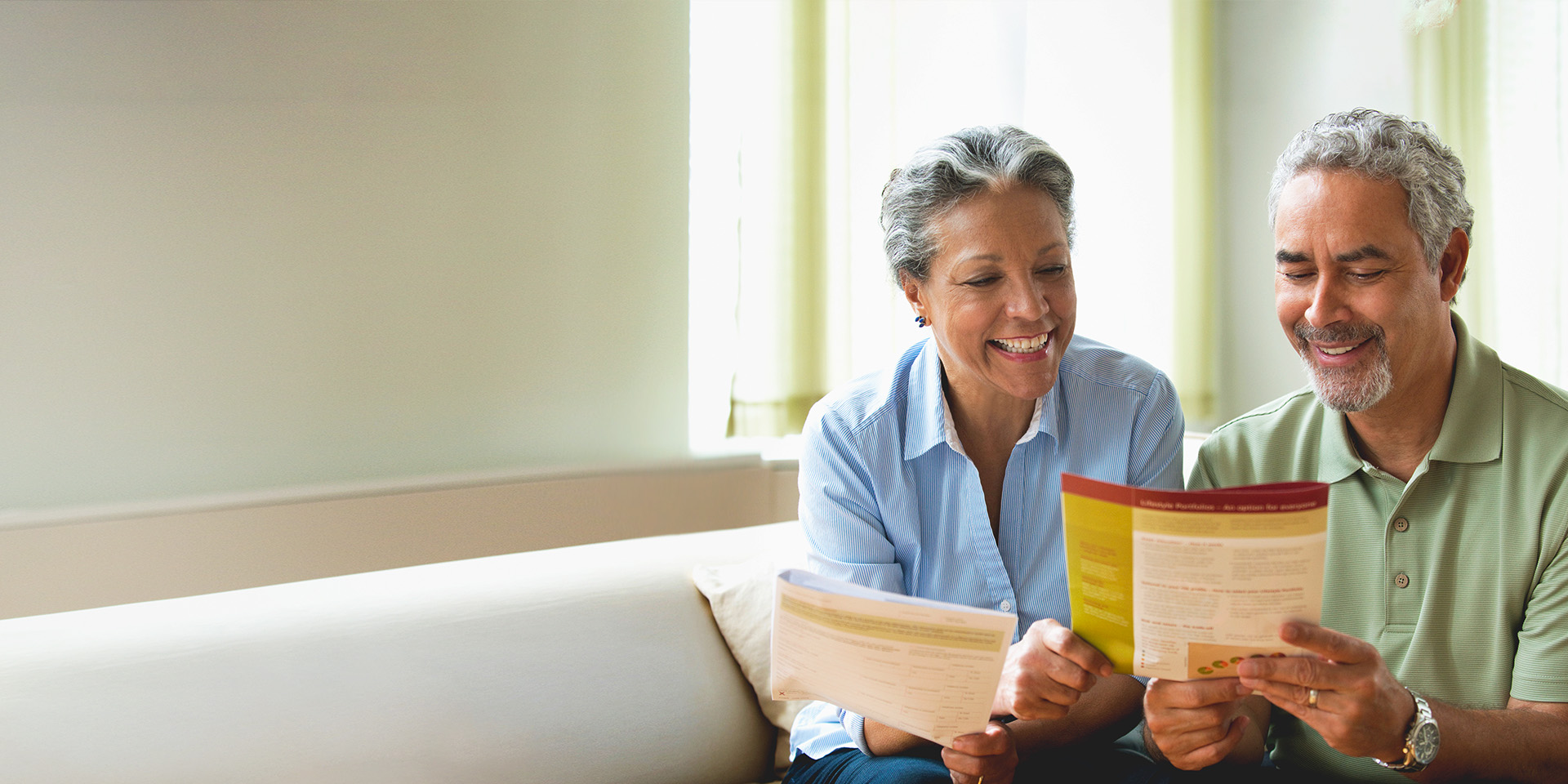 Older couple sits on a couch in a bright room, browsing through estate planning pamphlets together.