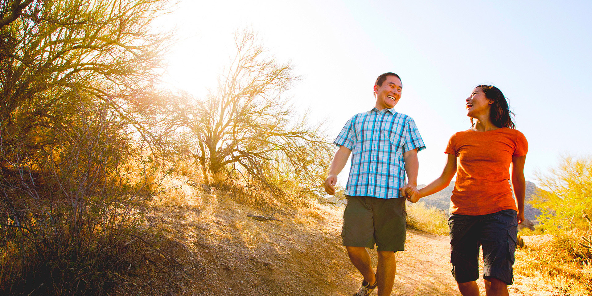 Happy couple holding hands while walking down a trail in the desert. 