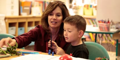 A 1 Darn Cool School teacher providing hands-on guidance to a young student, kneeling down, as they explore and create together during a classroom project.