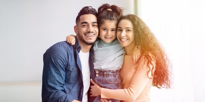 From left to right: a young man, a young girl, and a young woman all hugging each other and smiling for the camera.