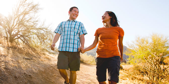 Happy couple holding hands while walking down a trail in the desert. 