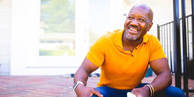 Joyful older adult male sitting on the front porch steps holding his mobile device.