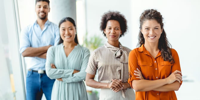 Facing the camera, a cohesive team of four employees stands diagonally in the office, projecting confidence and unity.