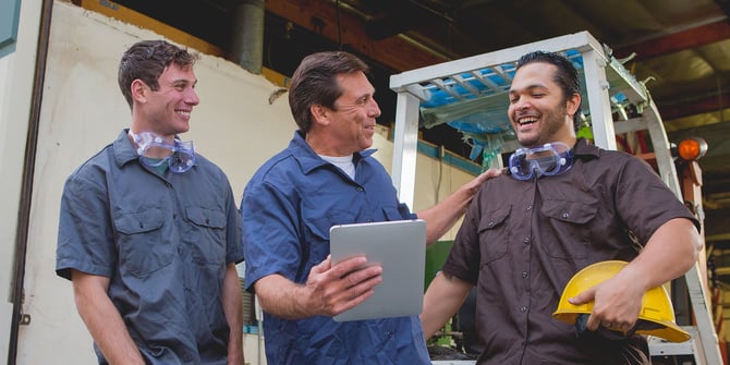 Three construction workers surrounding a tablet and celebrating how MyMoney@Work benefits their company and employees.